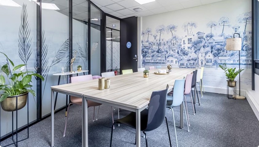 Salle de réunion aménagée au sein du Trigone B’Coworker à Angers, avec grande table, chaises colorées et décoration murale.