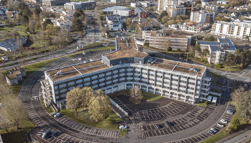 Vue aérienne du bâtiment Trigone B’Coworker à Angers, avec parkings, espaces verts et environnement urbain.