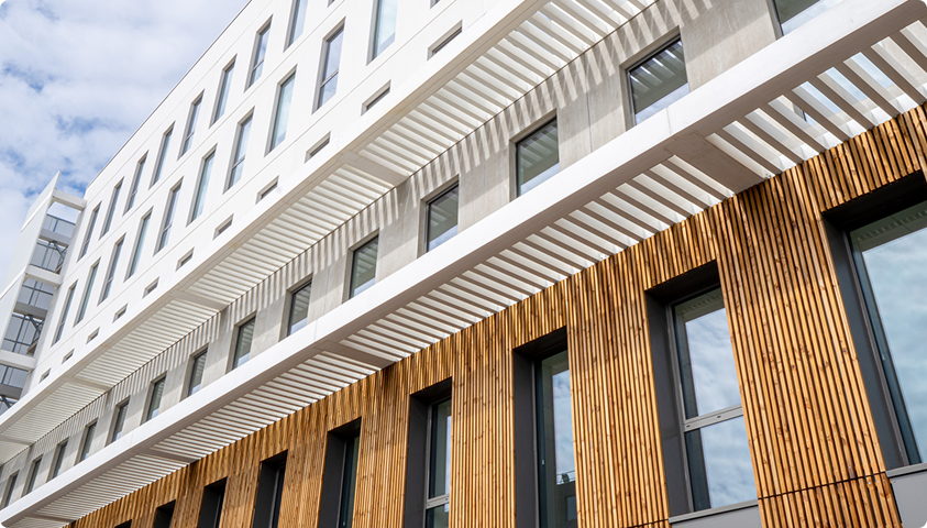Vue en contre-plongée de la façade du bâtiment A du SPI, associant bardage bois, béton clair et brise-soleil.