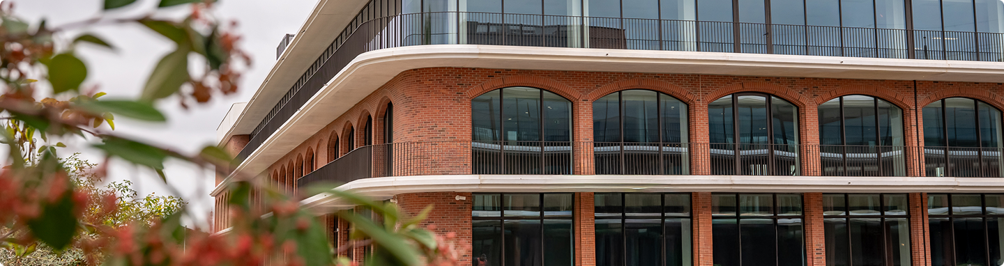 Vue rapprochée de la façade de l’Imaginarium, avec arches en briques, balcons filants et grandes surfaces vitrées.