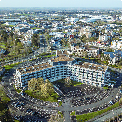 Vue aérienne du bâtiment Le Trigone, projet de FSDV, avec parkings, espaces verts et environnement urbain.